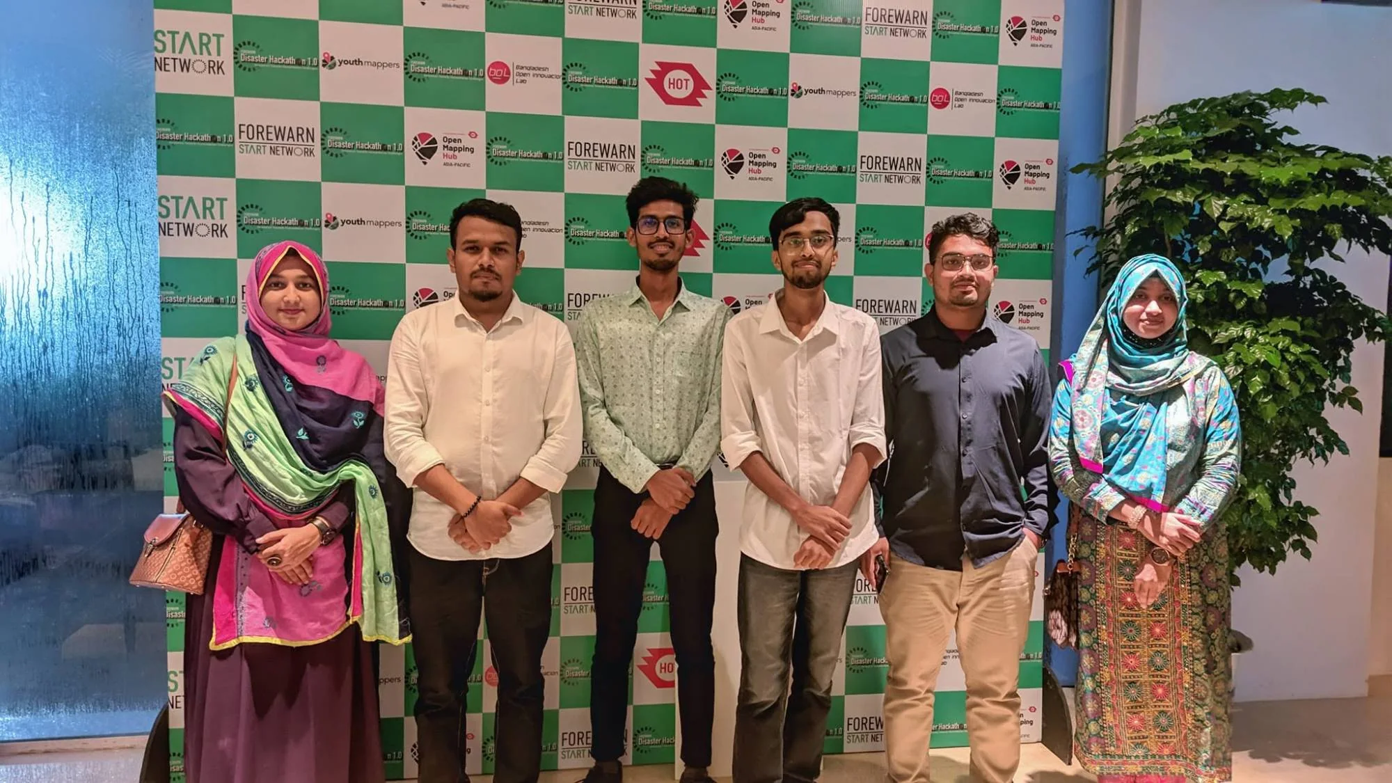 Six team members standing in front of the FOREWARN Disaster Hackathon 1.0 sponsor wall